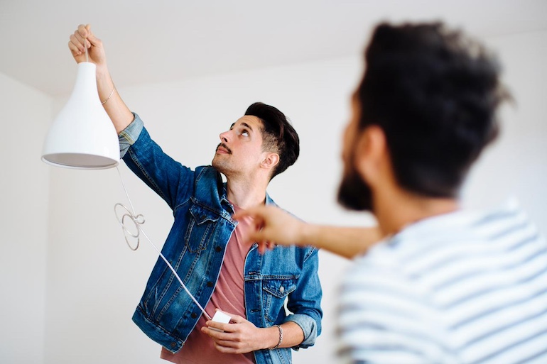 Ein Mann hält eine Deckenlampe hoch, die noch nicht angeschlossen ist, ein anderer ist von hinten zu sehen