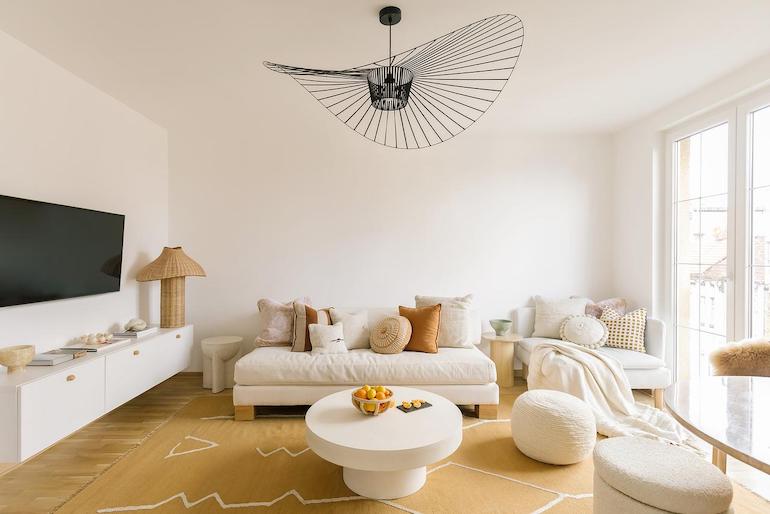 Helles neutral eingerichtetes Wohnzimmer mit Sofa, Tisch, TV und Hockern