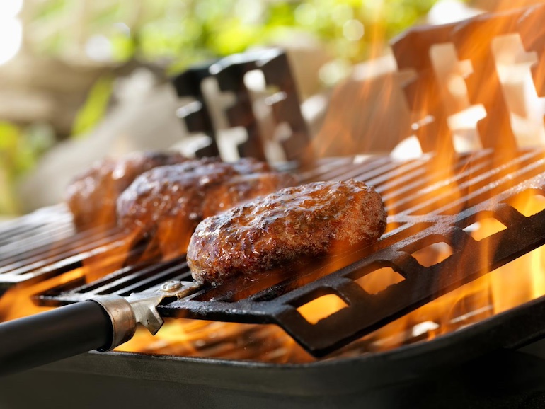 Ein schwarzer Grill von Nahem, Flammen umspielen das Grillgut