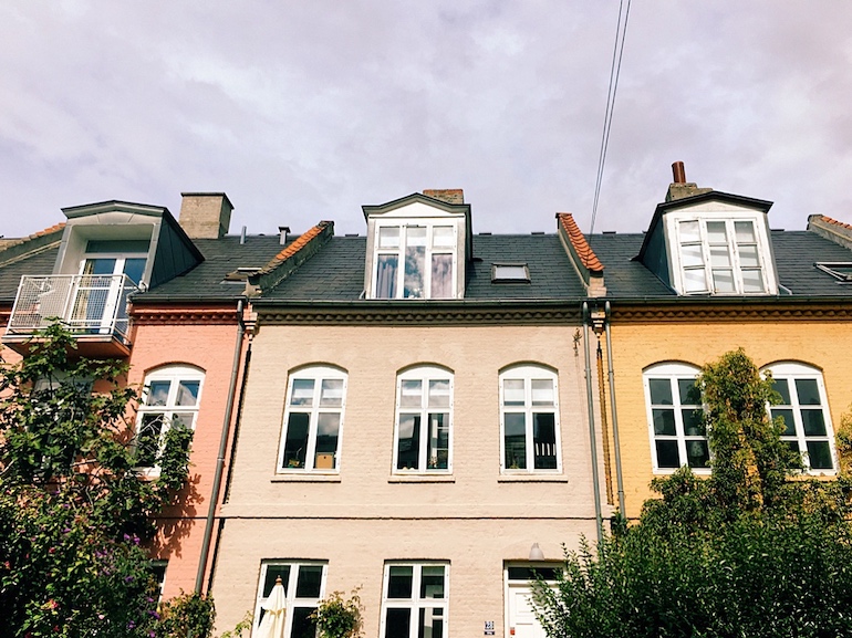 Bunte Häuserreihe vor Bäumen von Unten fotografiert, wodurch die Linien nach oben optisch spitz zulaufen