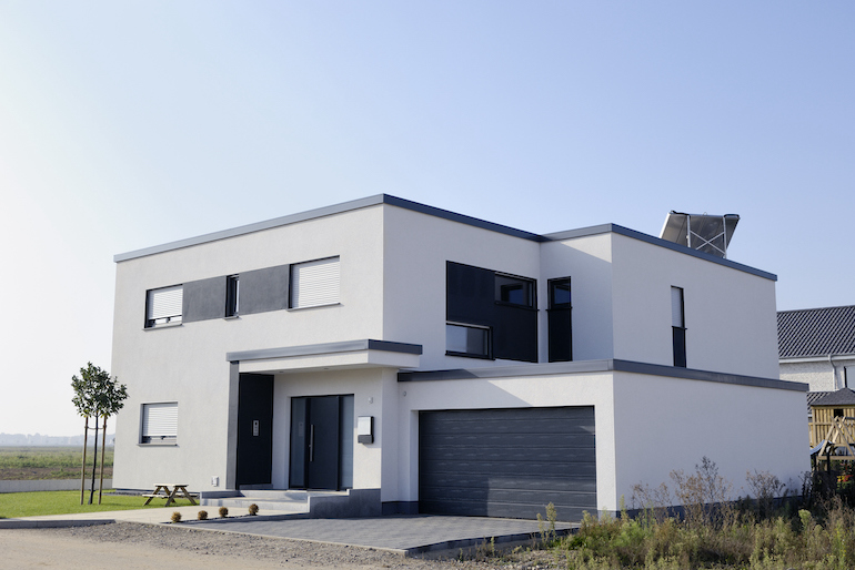 Modernes Haus mit geradem Dach und Garage, schräg von der rechten Seite fotografiert bei Sonnenschein
